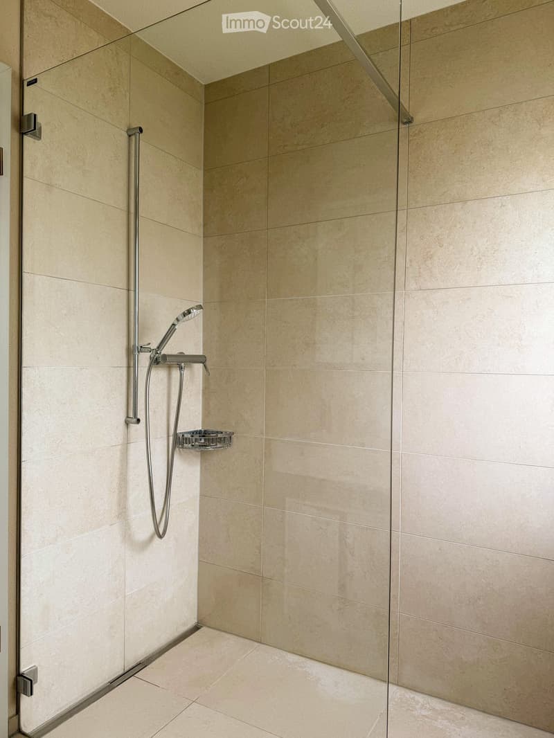 Modern bathroom with a glass shower enclosure, beige tiles, and a silver shower head.