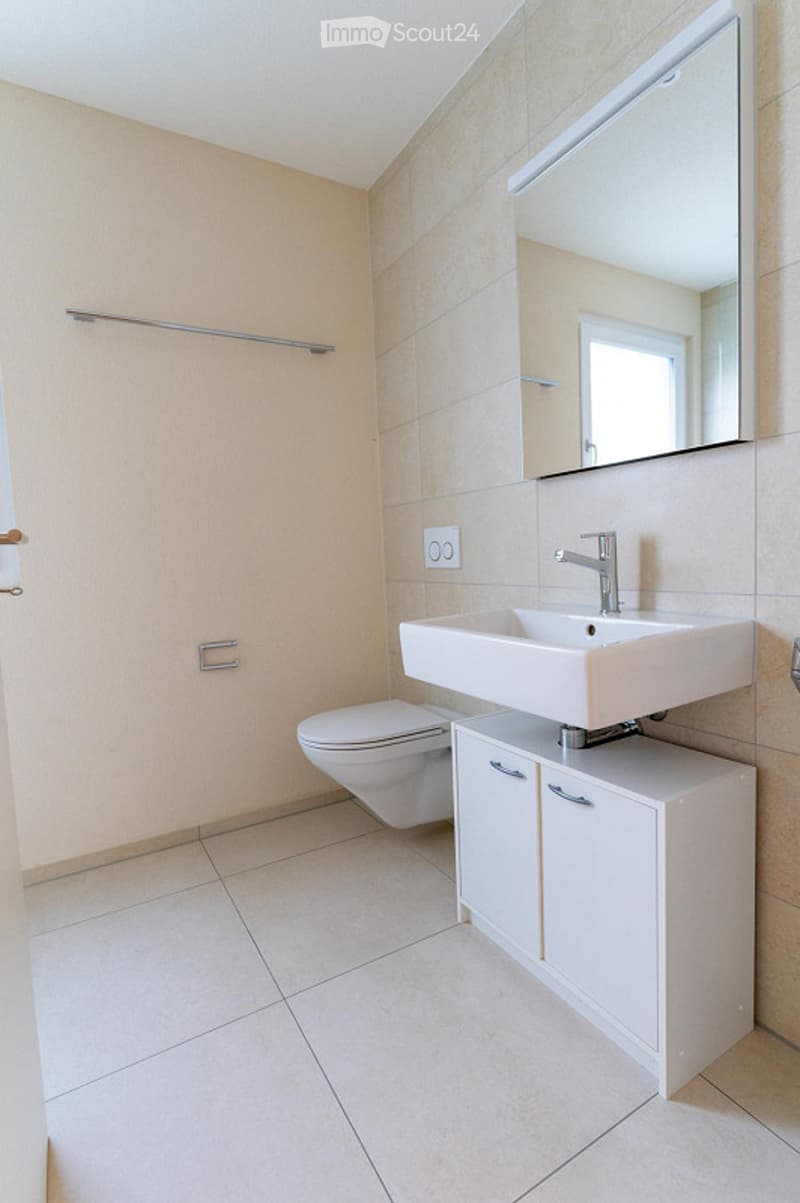 Modern bathroom with a white sink, toilet, and cabinet. Features a large mirror above the sink and tiled walls and floor.