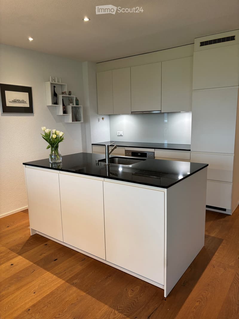 modern kitchen with white cabinets, black granite countertop, stainless steel sink, faucet, white flowers in vase, wooden floor