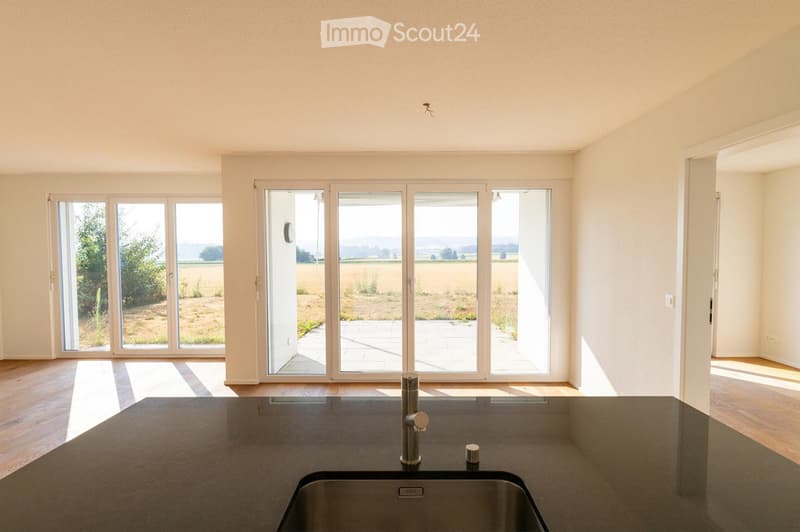 Modern kitchen with large windows offering a scenic view, featuring a central island with a sink and faucet.