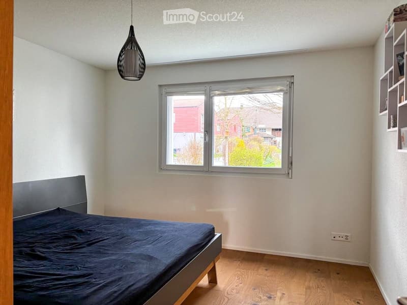A simple bedroom with a bed, a lamp, and an outlet on the wall.