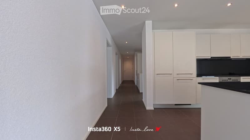 Modern hallway with white walls, dark brown tiled floor, and white cabinetry visible on the right side.