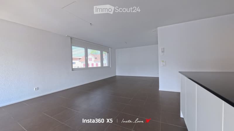 Empty room with white walls, dark tiled floor, and large window with blinds. No furniture or equipment present.