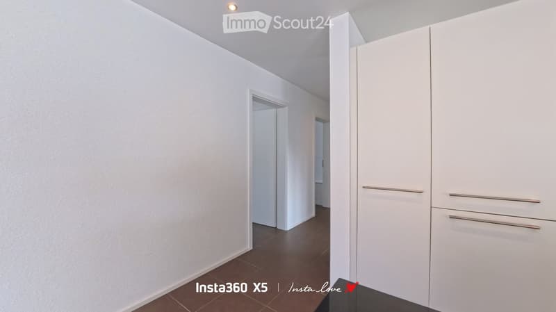 Empty hallway with white walls, dark tiled floor, and a white closet with silver handles on the right side.