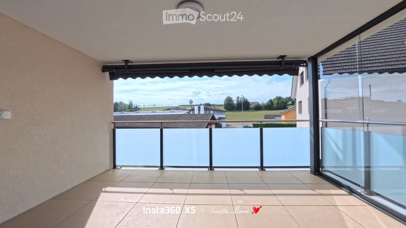 Spacious balcony with tiled floor, glass railing, and a retractable awning, offering a scenic view of the surrounding landscape.