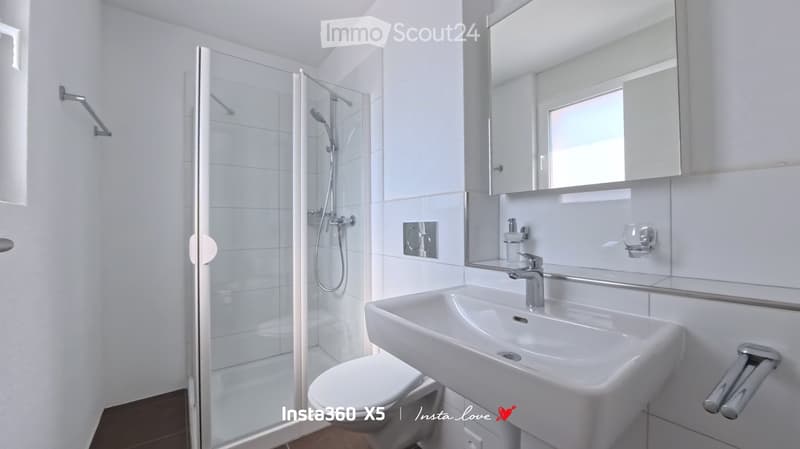 Modern bathroom with white tiles, a glass-enclosed shower, a white sink with a chrome faucet, and a toilet.