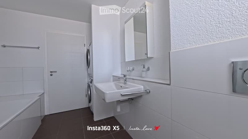 Modern bathroom with white tiles, a sink, mirror, bathtub, and a door leading to a washing machine area.