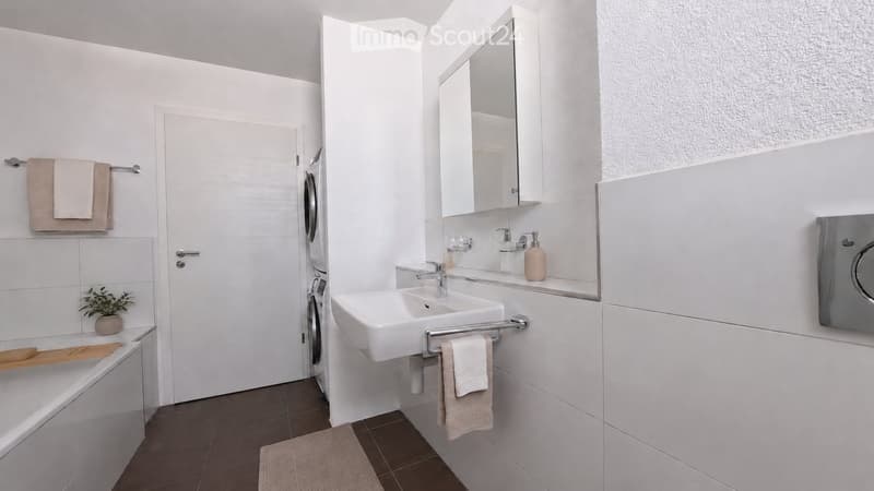 Modern bathroom with white tiles, a bathtub, a sink with a mirror cabinet, and a towel rack with towels. A small plant is placed on the edge of the bathtub.
