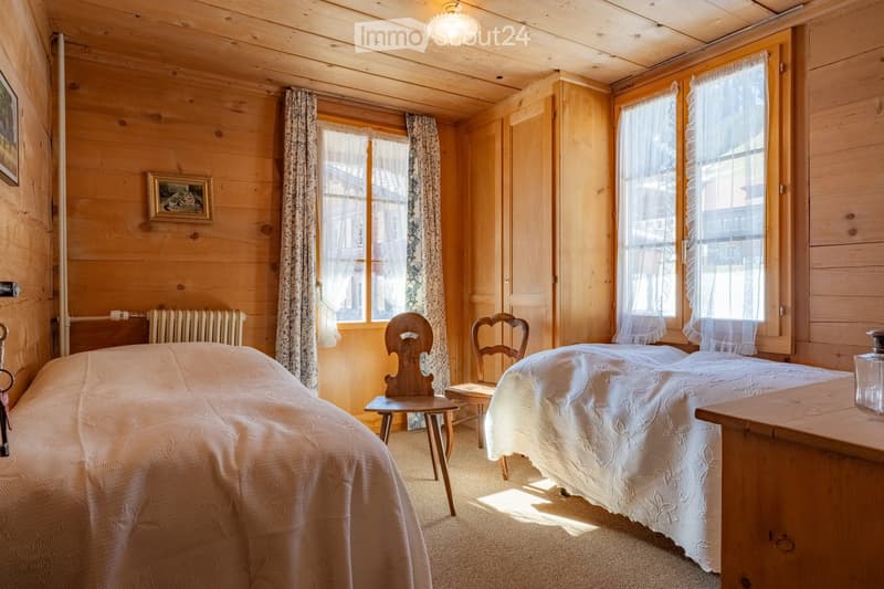 Cozy wooden bedroom with two single beds, wooden chairs, radiator, and framed picture on wall.
