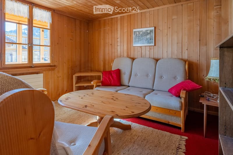Cozy living room with wooden walls and ceiling, featuring a grey sofa with red cushions, a wooden coffee table, a wooden side table, a chair, and a picture frame on the wall.