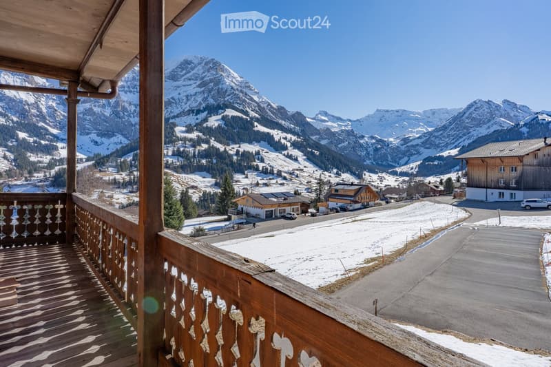 Balcony overlooking a snowy mountain landscape with a village below, wooden railing, clear blue sky.