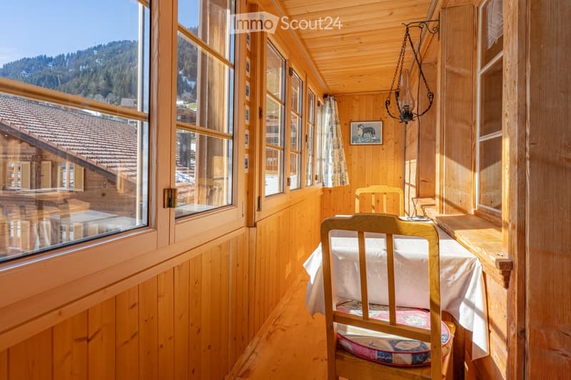 Cozy wooden balcony with a view of the surrounding landscape, featuring a wooden chair, small table, and a chandelier.