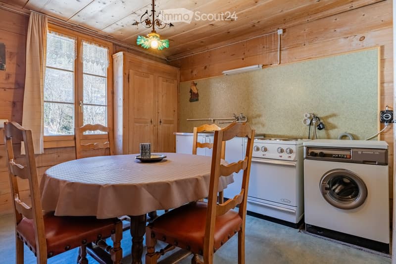 Cozy kitchen with wooden walls and ceiling, featuring a dining table with chairs, an oven, and a washing machine.