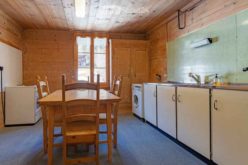 A cozy kitchen and dining area with wooden walls, a dining table with chairs, a refrigerator, a washing machine, and a sink with a faucet.