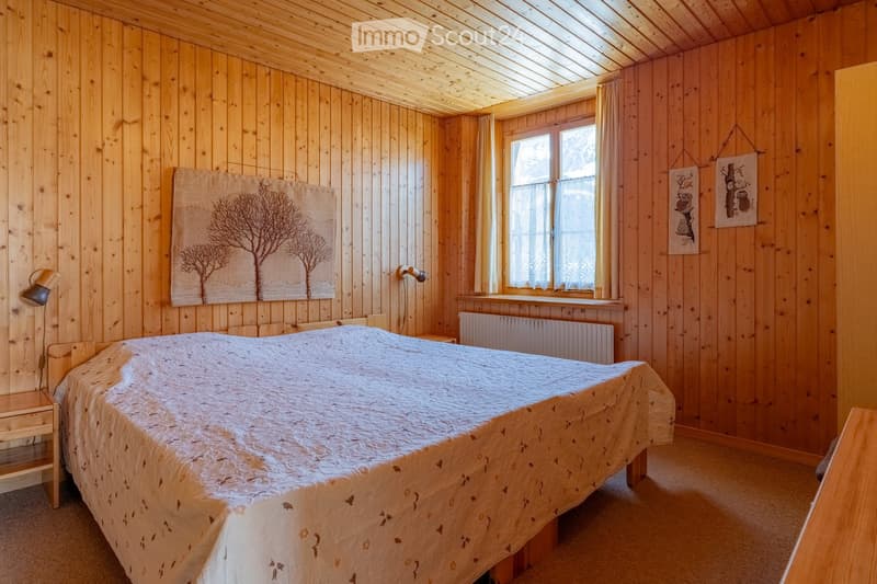 Cozy wooden bedroom with a large bed, nightstand, wall-mounted lamp, radiator, and decorative wall art featuring tree silhouettes.