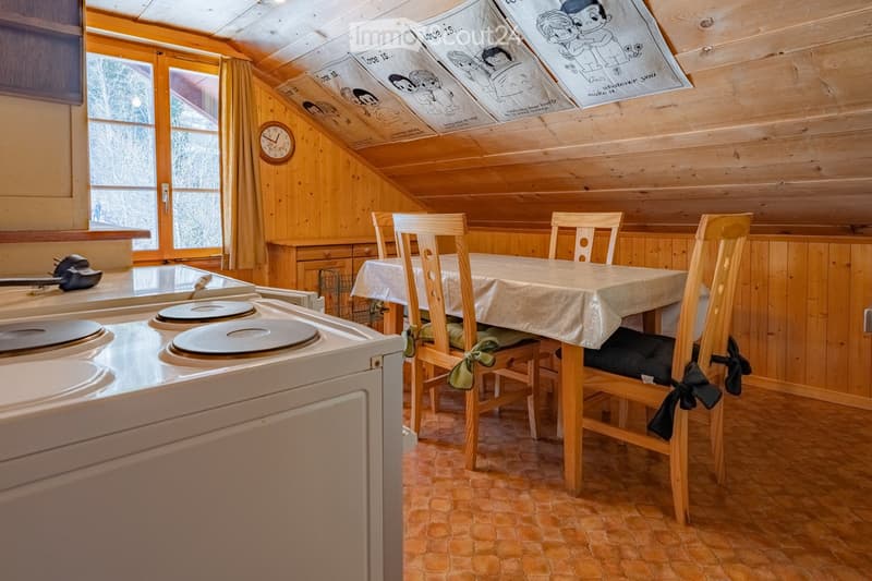 Cozy kitchen with wooden walls and ceiling, featuring a stove, dining table with chairs, and a clock on the wall.