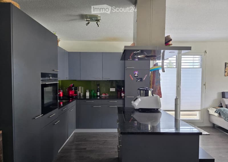 Modern kitchen with grey cabinets, stainless steel appliances, and a central island with a black countertop.