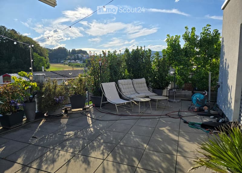 Balcony with tiled floor, two white lounge chairs, small table, potted plants, and outdoor lighting string.