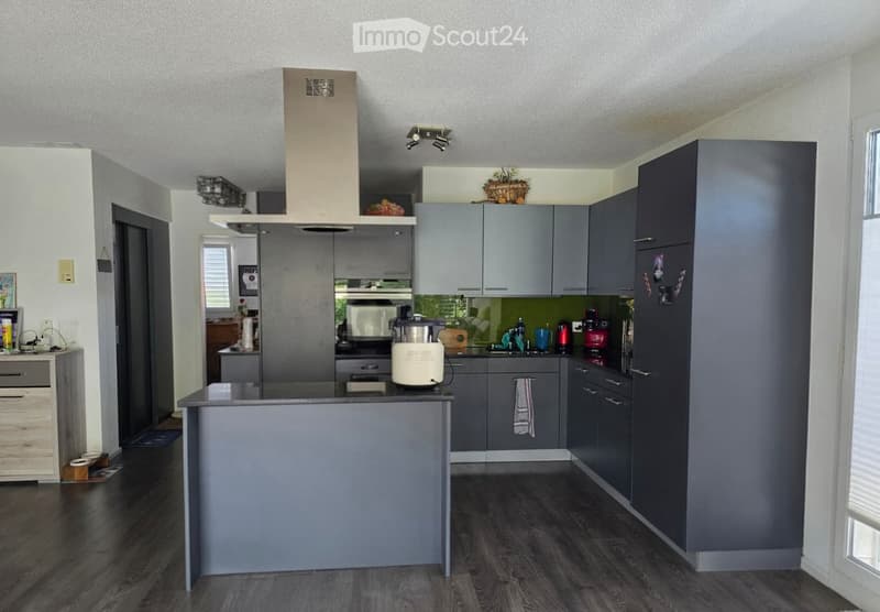 Modern kitchen with grey cabinets, stainless steel appliances, and a central island. Features include a refrigerator, oven, microwave, dishwasher, coffee maker, blender, and various kitchen utensils.