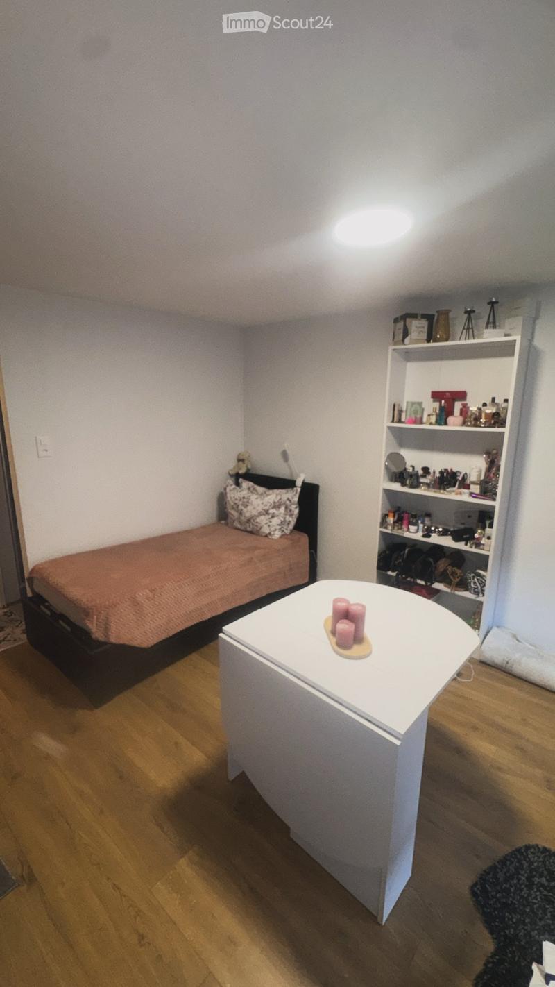 Cozy bedroom with a single bed, a small white table with candles, a shelf filled with various items, and a mirror on the wall.