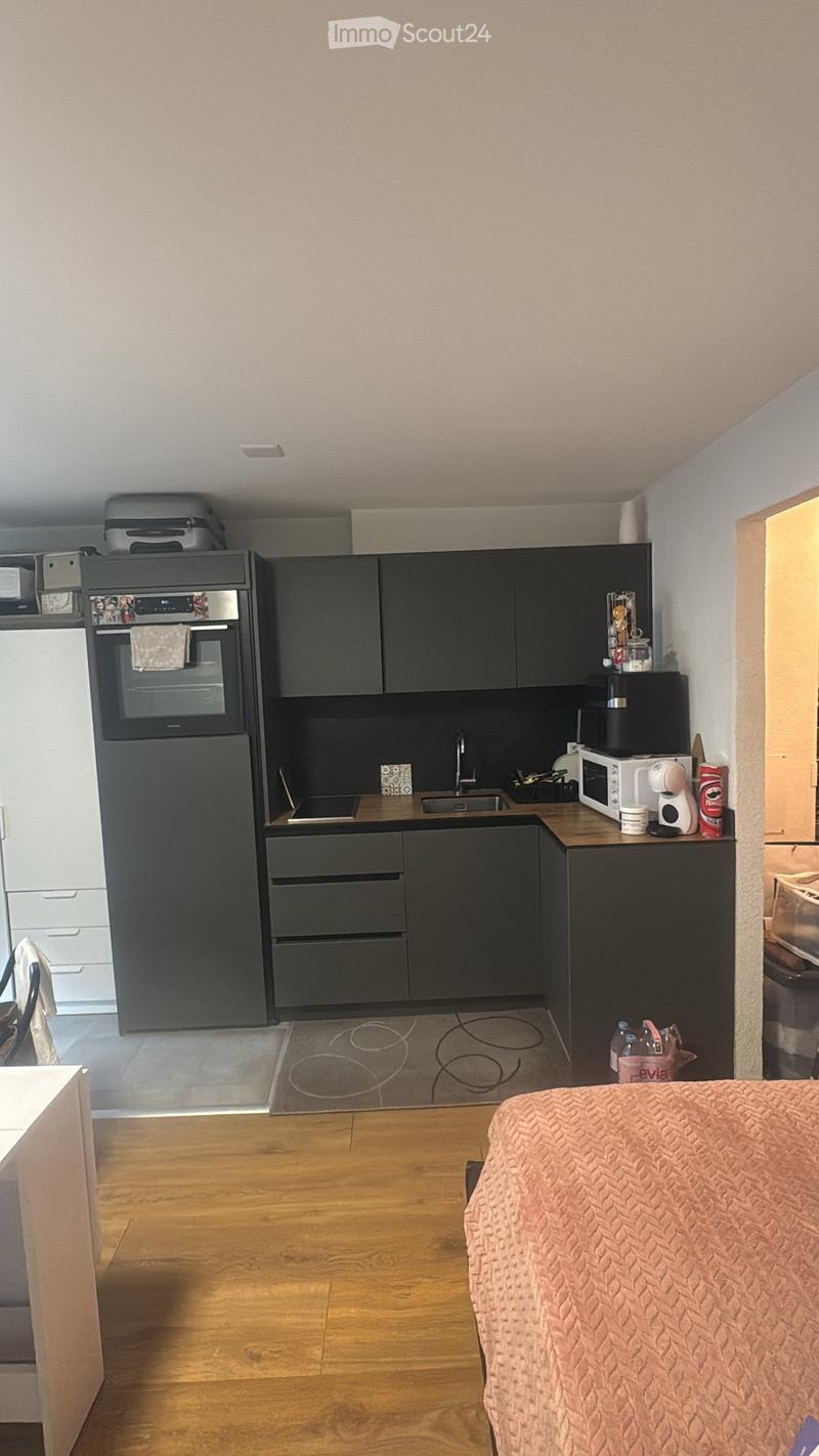 Modern kitchen with dark grey cabinets, stainless steel appliances, and a small dining area with a pink cushioned chair.