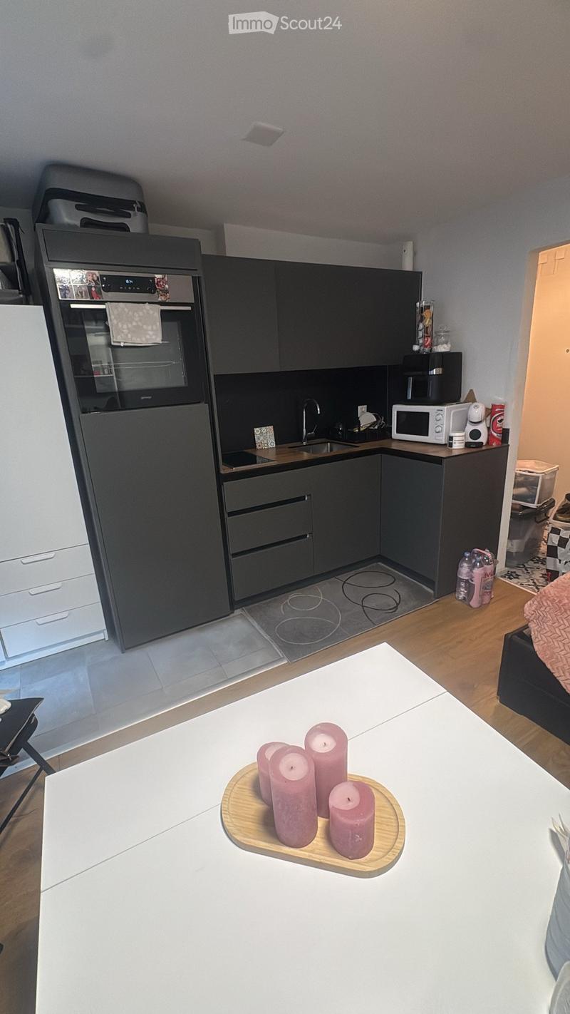 Modern kitchen with dark grey cabinets, stainless steel oven, microwave, sink, and a white dining table with pink candles.