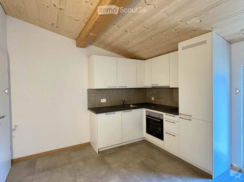 Modern kitchen with white cabinets, a sink, and an oven, featuring a wooden slanted ceiling and tiled floor.