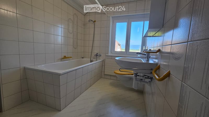 Bathroom. Bathroom with white tiles, bathtub, toilet, sink, and shower head. The window offers a view of the outdoors.