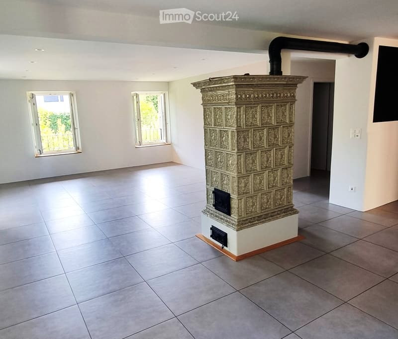 Empty room with tiled floor, white walls, two windows, and a decorative fireplace with a black chimney pipe.