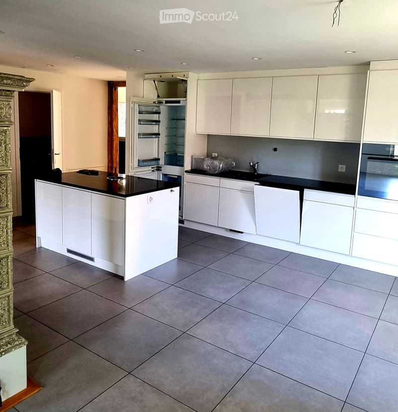 Modern kitchen with white cabinets, black countertops, and a central island. Features include a stainless steel refrigerator, oven, and sink.