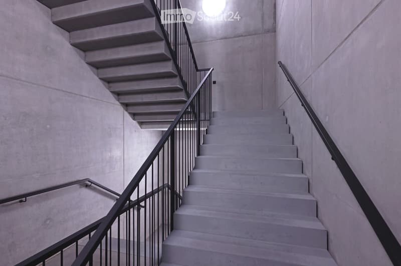 Modern concrete staircase with sleek black metal railings and a bright overhead light fixture.