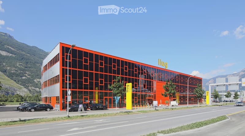 Modern, multi-story building with orange and black facade, large glass windows, and a parking area with several cars.