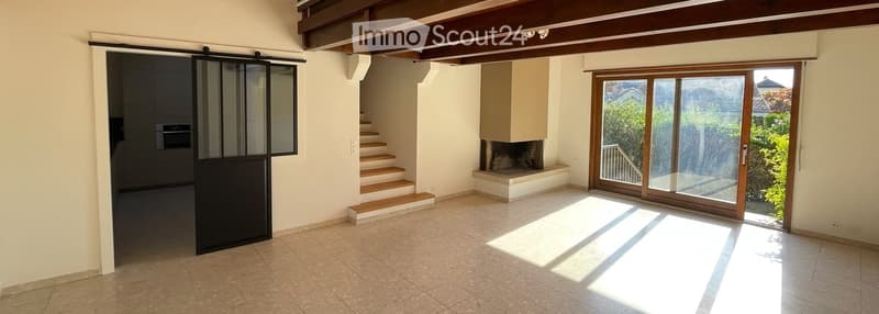 Empty room with tiled floor, white walls, wooden ceiling beams, sliding glass door leading outside, staircase, and fireplace.