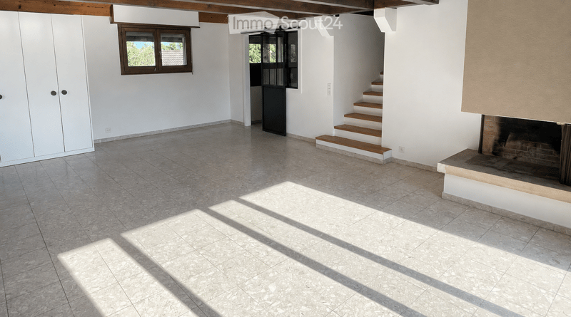 Empty room with tiled floor, white walls, wooden ceiling beams, staircase leading to another level, and a fireplace area.