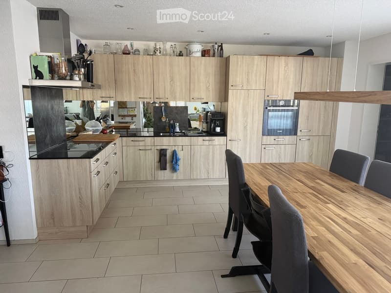 Modern kitchen with light wood cabinets, a central island, and a dining area featuring a wooden table and chairs.