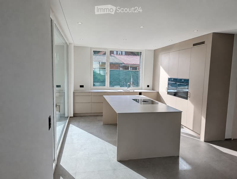 Modern kitchen with a central island, light-colored cabinets, and a large window overlooking a patio.