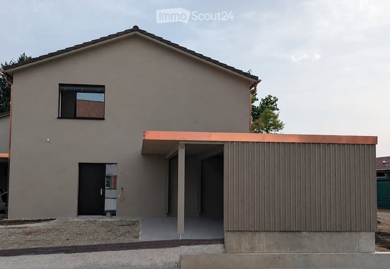 Modern single-story house with a raised ground floor, grey facade, copper roof accents, and a covered entrance area.