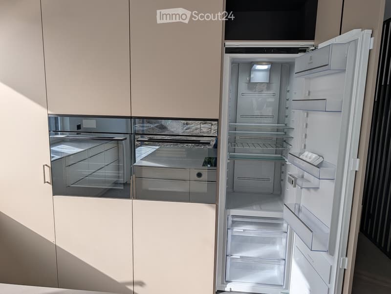 Modern kitchen with light-colored cabinets and an open refrigerator, showcasing its interior compartments and shelves.
