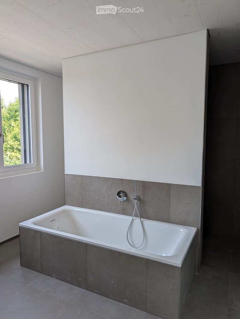 Modern bathroom with a white bathtub, grey tiled walls, and a sleek chrome faucet.