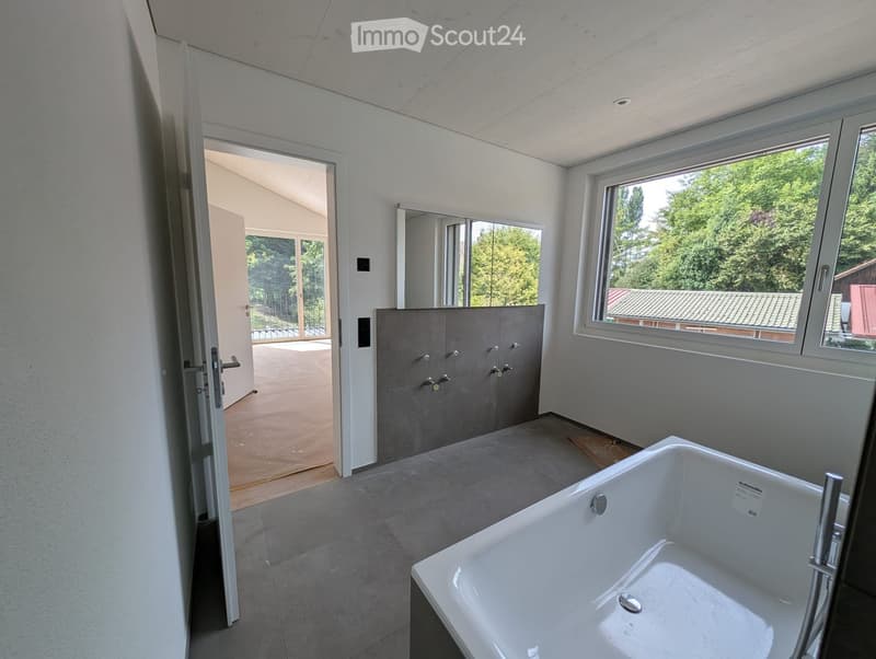 Modern bathroom with a large bathtub, sleek cabinetry, and large windows offering a view of greenery.