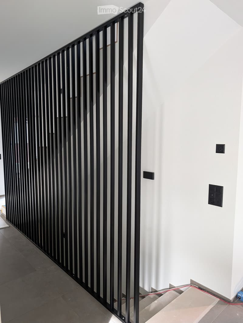 Modern hallway with white walls, dark tiled floor, and a black metal railing leading to an upper level.