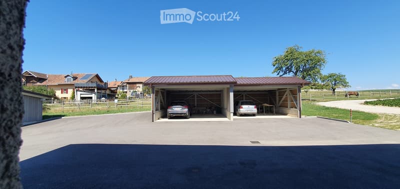Detached garage with two cars parked inside, located in a rural setting with neighboring houses and a fenced area.