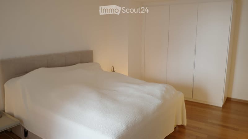 A modern bedroom with a neatly made bed, a large wardrobe, and light wooden flooring.