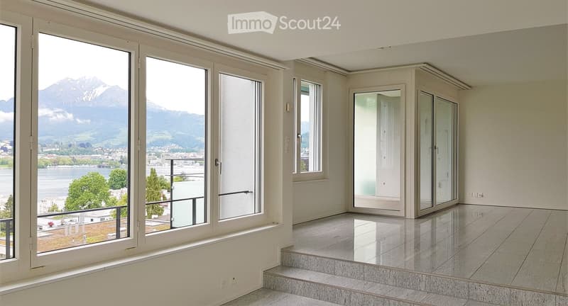 Empty room with large windows offering a scenic mountain and lake view, polished tile floor, and a small step leading to a balcony area.