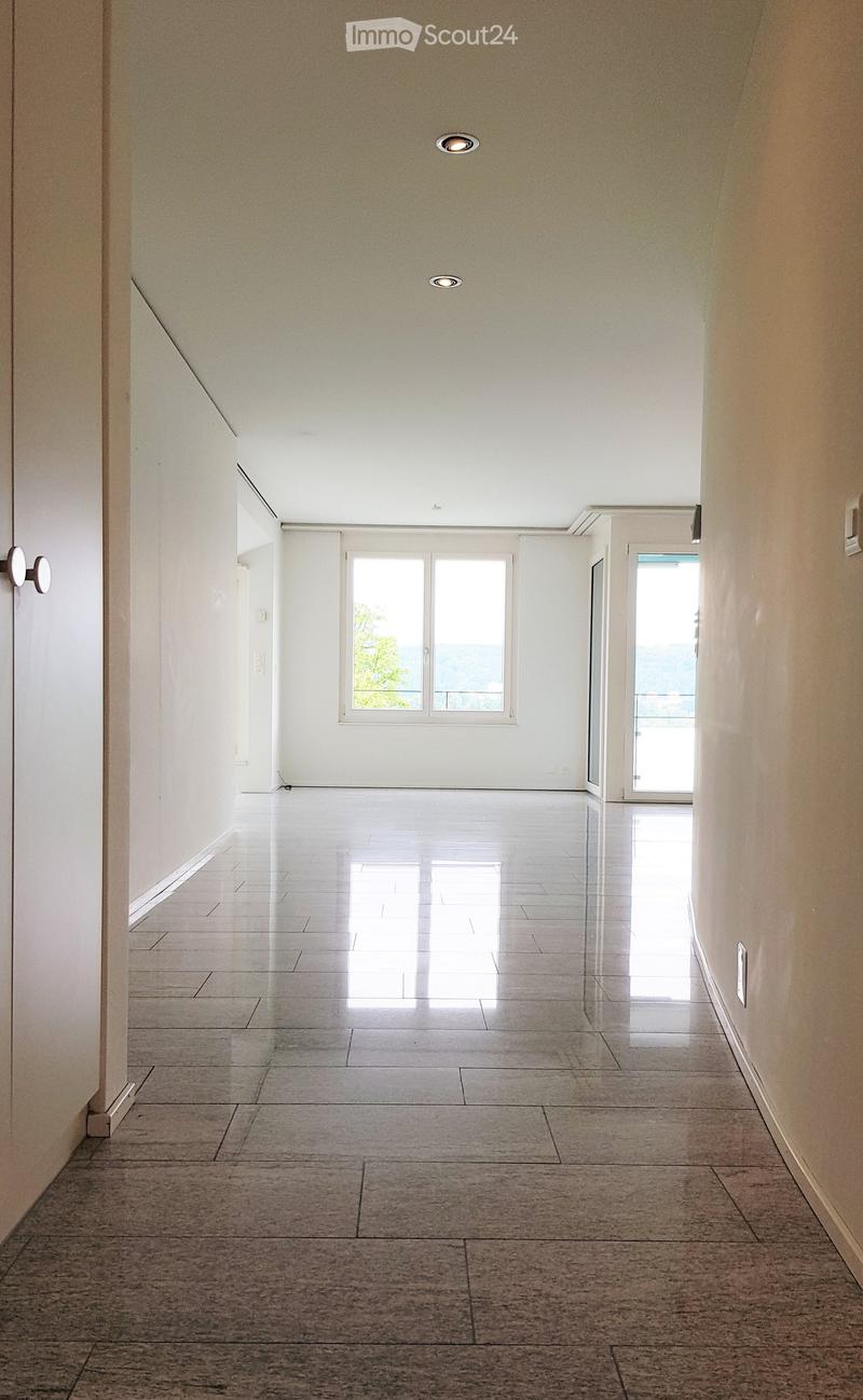 Empty hallway with white walls, polished tile floors, and recessed lighting. Features a window and a glass door leading to an outdoor area.