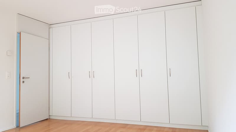 Empty room with white built-in wardrobes, light wooden flooring, and a partially open door leading to another space.