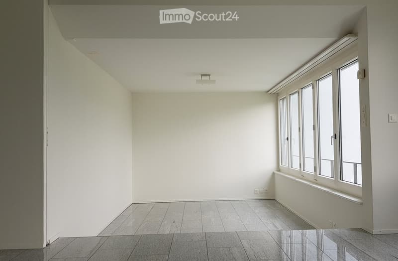 Empty room with white walls, tiled floor, large windows, and modern lighting fixture.