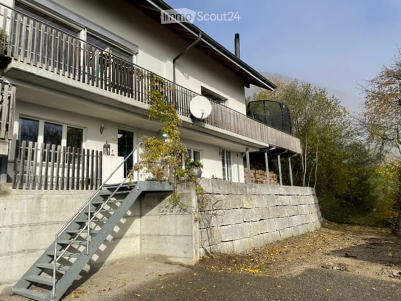 Two-story house with white exterior, multiple balconies, satellite dish, and a staircase leading to the entrance.