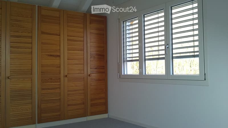 Empty room with wooden closet doors and windows with blinds. No furniture or equipment present.
