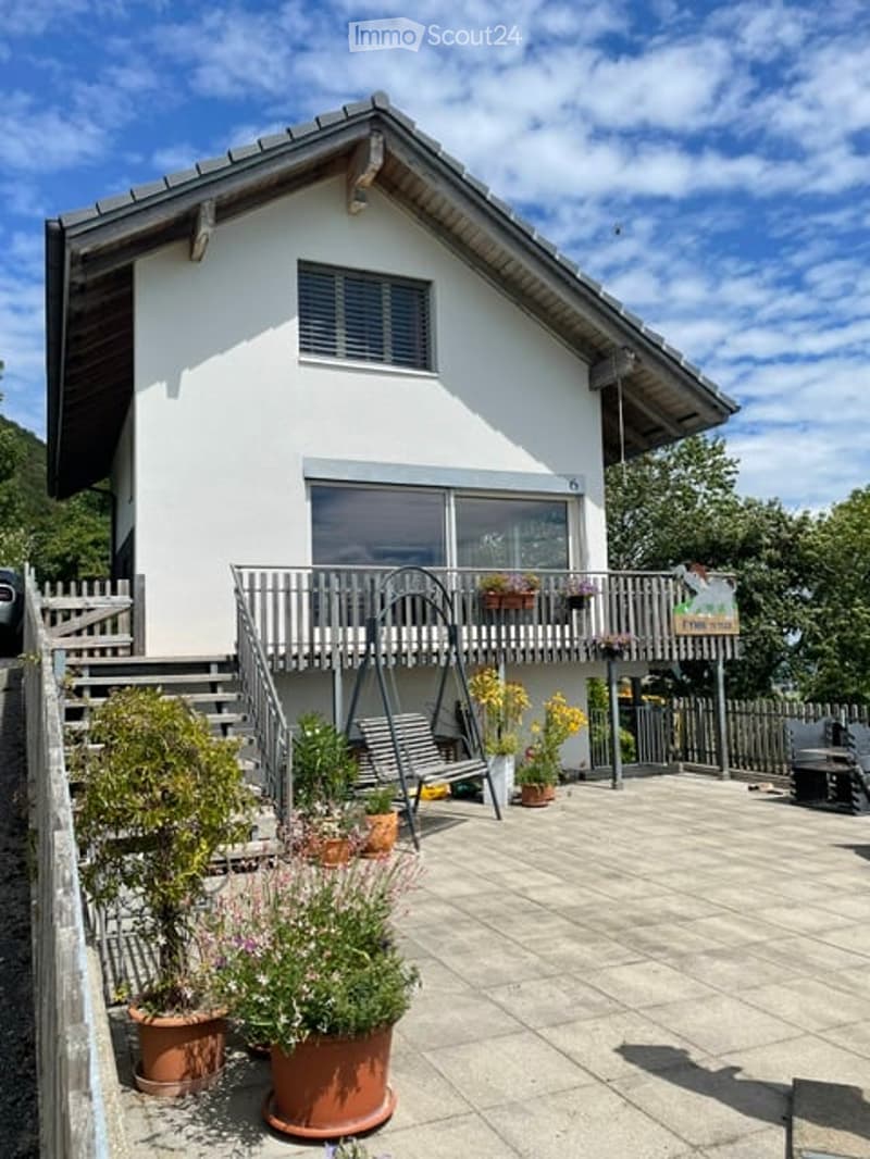 Single-story house with white exterior, large balcony, and potted plants on the patio.